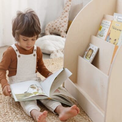 Lapsi lukee lastenkirjaa KUMPU kirjahyllyn vieressä valoisassa huoneessa